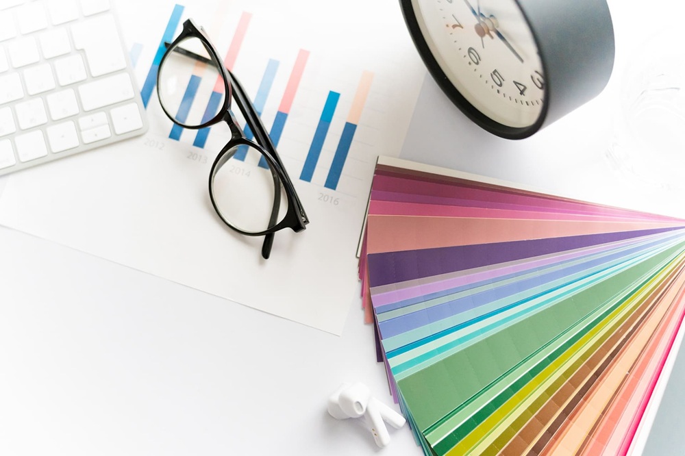 デスクにある色見本とメガネと置き時計、棒グラフ資料