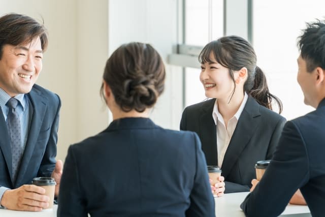 窓のある明るい職場で和やかに談笑する男女4名の従業員