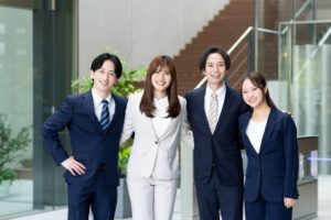 肩を組んでいるスーツ姿の男女4人グループ