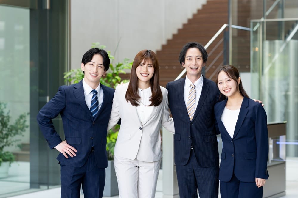 肩を組んでいるスーツ姿の男女4人グループ