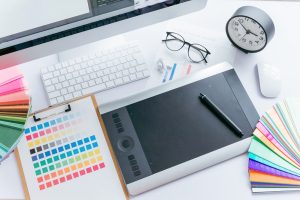 タブレットや色見本、小さな置き時計やPCが置かれている作業デスク