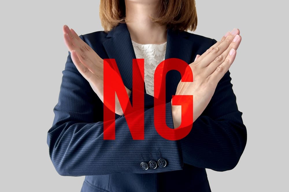 腕でバツを作っているスーツの女性