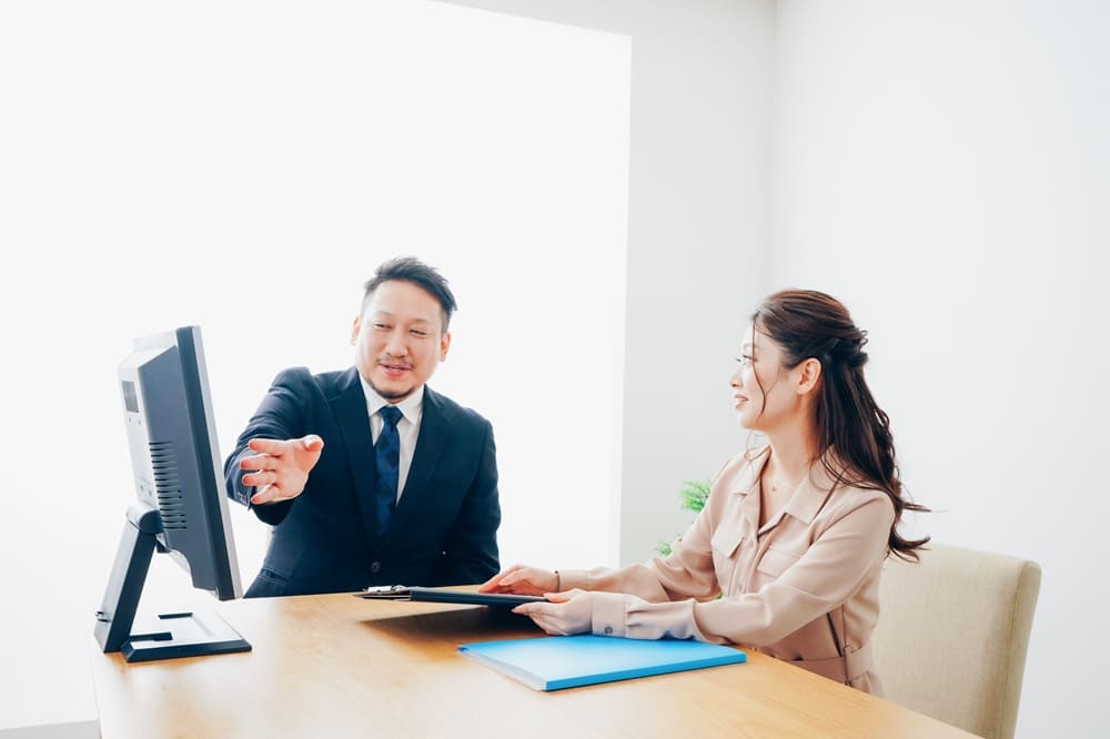 マンツーマンでPCを見ながら指導するスーツの男性と教わるシーツの女性