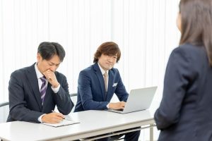 採用面接で渋い表情をしている2人の男性面接官と手前に女性の求職者