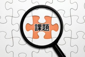 パズル内でピースがブランクの箇所に「課題」という文字、その文字を囲むように置かれた虫眼鏡