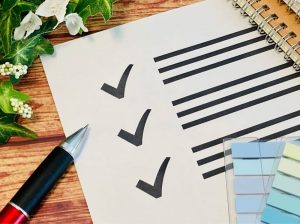 チェック項目とそれを囲むように置かれたボールペンと付箋、ノート
