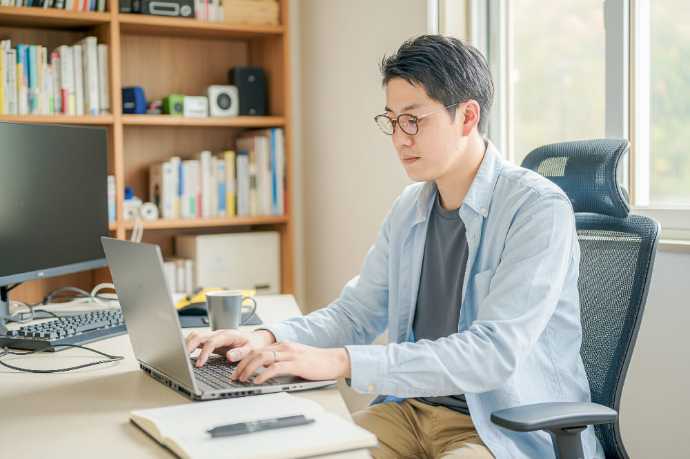 明るい自室で仕事をしているメガネをかけた30代の男性