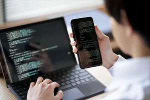 ノートパソコンとスマートフォンでプログラミングのコードを確認するプログラマー