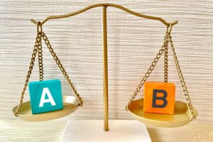 制作会社や派遣など依頼先による費用の違いを比較する、AとBのブロックが乗った天秤