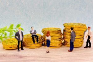 デザイン依頼の相場や予算組みをイメージした、積み上げられたコインと複数人のビジネスパーソンのミニチュア