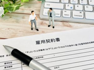 雇用契約書とパソコンのキーボードの上に立つビジネスパーソンのミニチュア