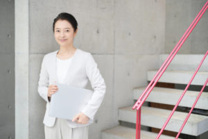 スーツ姿でノートPCを小脇にかかえた、転職に成功したUIデザイナーの50代女性