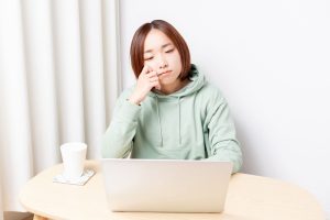 ノートPCを眺めながら頬杖をつくパーカーを着たショートカットの女性