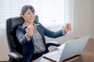 ノートPCを前に両手でガッツポーズをするビジネスウーマン