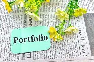 「portfolio」と書かれたエメラルドグリーンのメモ、背景は英字新聞
