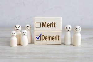 「Merit」「Demerit」と記載された積み木「Demerit」にチェックマークが入っており周囲の複数の人形が残念そうな表情をしている