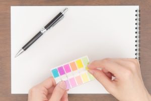 ノートに付箋を貼ろうとしている手と左上にペン