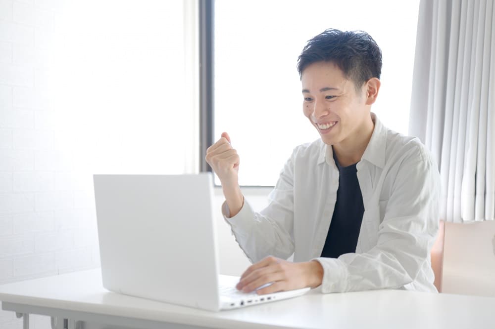 ノートパソコンを前にガッツポーズをしている男性