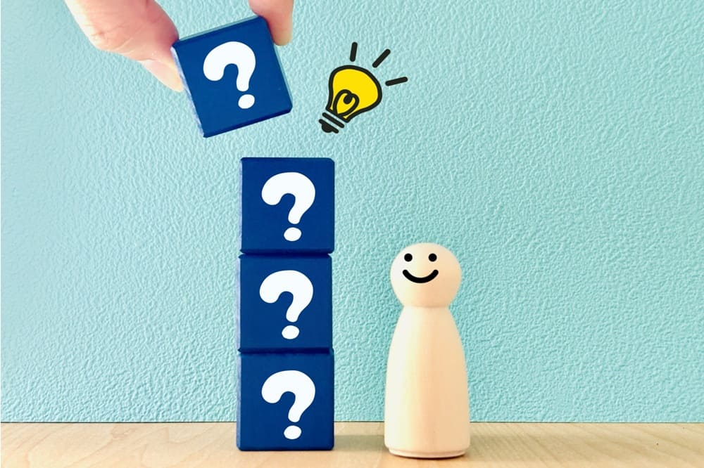 「?」が描かれた4つの積み木を見上げてひらめいている人形