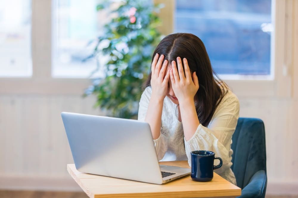ノートパソコンを前に両手で顔を覆っている女性
